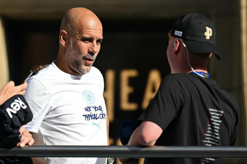 Departing Manchester City manager Pep Guardiola hops onto the bus with his youth players at the start of the winner's parade by the Manchester City team after their victories in the two domestic cup competitions on May 25, 2026, in central Manchester, north-west England.  Paul ELLIS / AFP