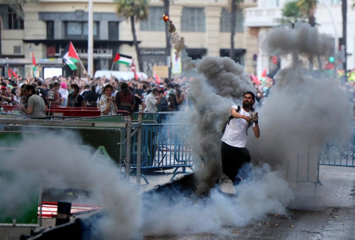 A man throws a smoke flare back at police after Pro-Palestinians protestors invaded the street forcing race organisers to abandon the 21st and final stage of the Vuelta a Espana 2025, in Madrid on September 14, 2025. Thomas COEX / AFP