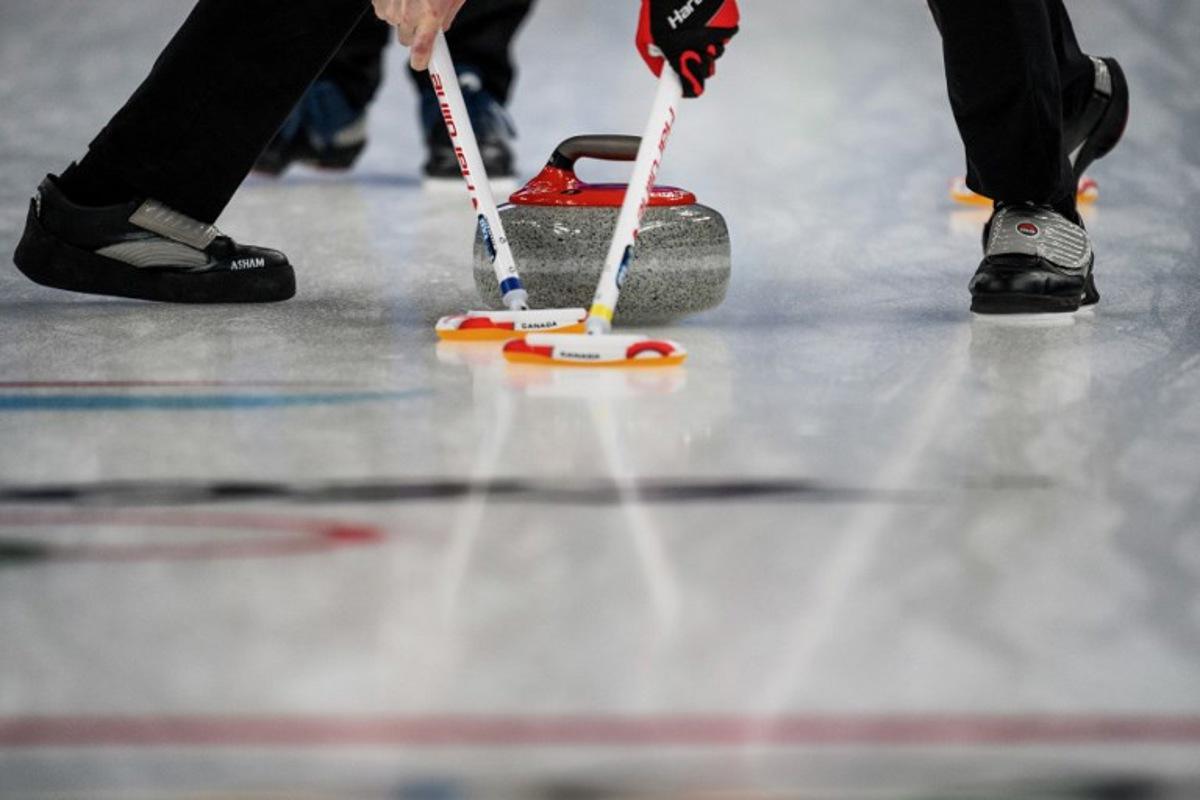 Competitors sweep in front of the curling stone during the men's bronze medal game of the Beijing 2022 Winter Olympic Games curling competition between Canada and USA at the National Aquatics Centre in Beijing on February 18, 2022. Jeff PACHOUD / AFP