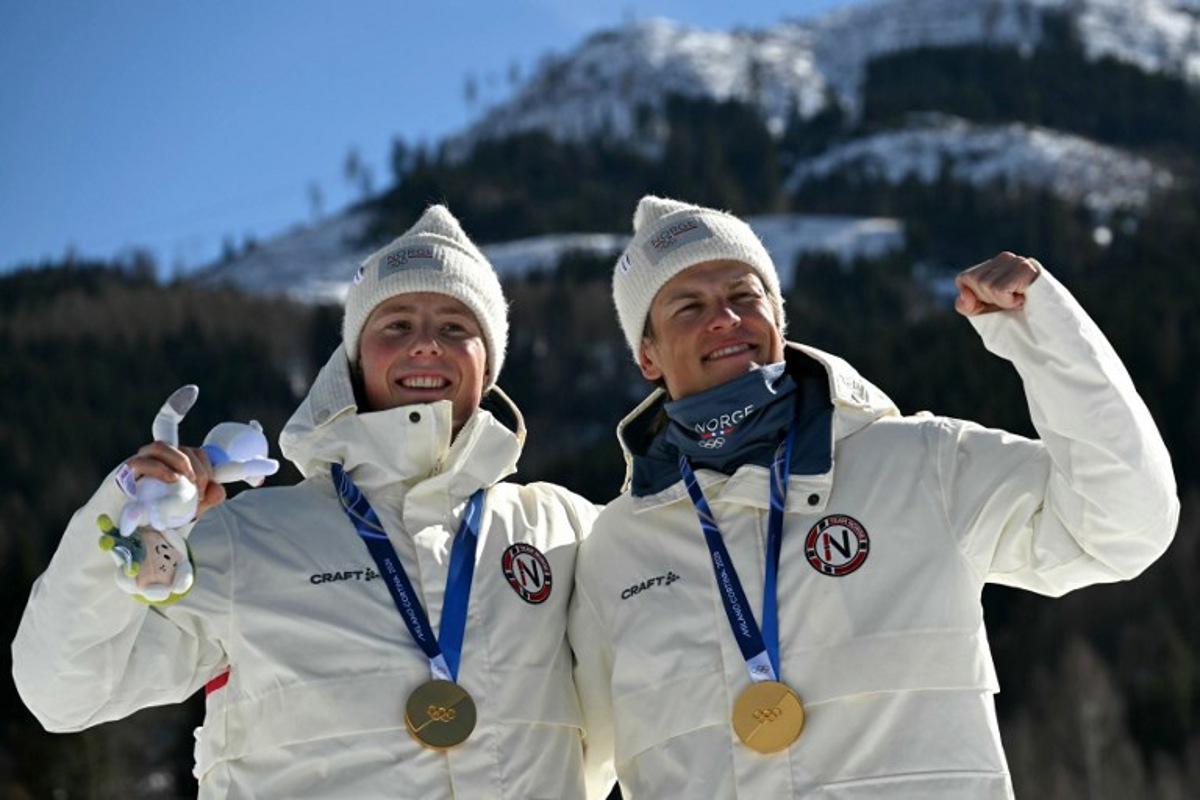 Gold medallists Norway's Johannes Hoesflot Klaebo (R) and Norway's Einar Hedegart celebrate on the podium for the men's team cross country free sprint final event of the Milano Cortina 2026 Winter Olympic Games at Tesero Cross-Country Skiing Stadium in Lago di Tesero (Val di Fiemme), on February 18, 2026. Javier SORIANO / AFP