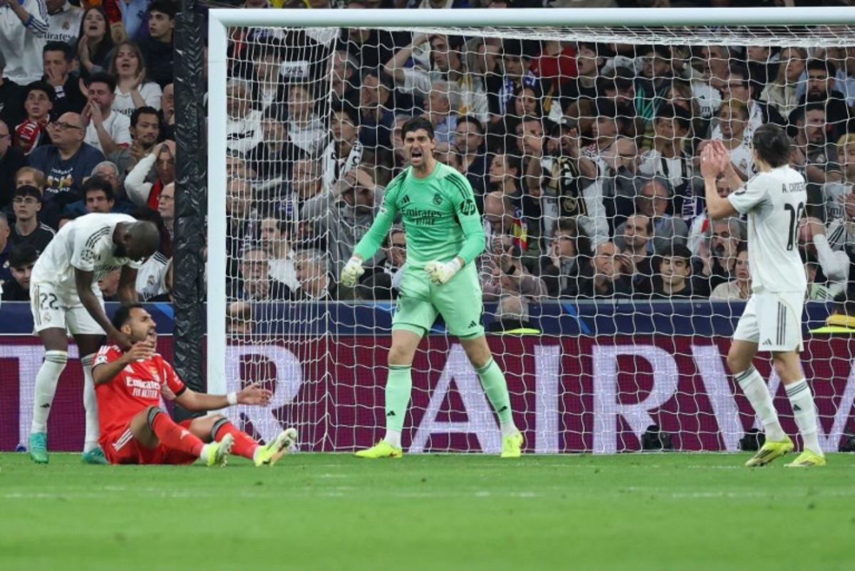 Real Madrid's Belgian goalkeeper #01 Thibaut Courtois reacts to saving the ball while Real Madrid's German defender #22 Antonio Ruediger talks with SL Benfica's Greek forward #14 Vangelis Pavlidis (L BOTTOM) during the UEFA Champions League knockout round play-off second leg football match between Real Madrid CF and SL Benfica at Santiago Bernabeu Stadium in Madrid on February 25, 2026. Thomas COEX / AFP