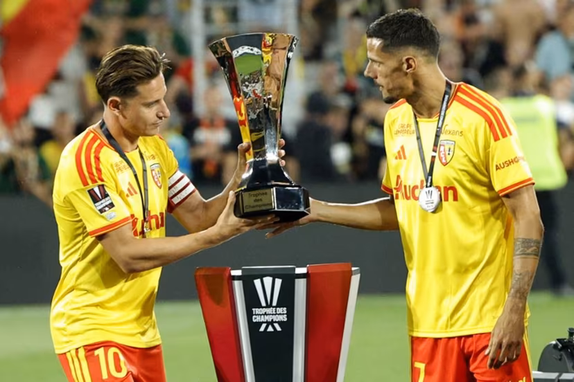 Lens' French forward #10 Florian Thauvin (L) and Lens' French forward #07 Florian Sotoca take the championship trophy to celebrate with teammates after winning the French Super Cup (Trophee des Champions) football match between RC Lens and Paris Saint-Germain (PSG) at the Stade Bollaert-Delelis in Lens, northern France on August 16, 2026. GEOFFROY VAN DER HASSELT / AFP