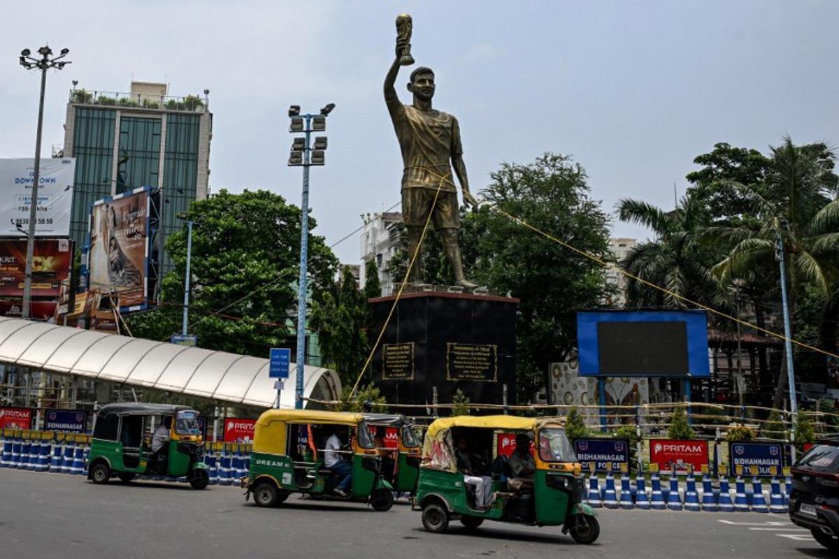 Rickshaws drive past a statue of Argentine football player Lionel Messi that has been tied with rope for stability from rain and thunderstorms, prior to its re-installation in a safer place, in Kolkata on May 27, 2026. Messi inaugurated the statue virtually during his visit to the city in December 2025. Dibyangshu SARKAR / AFP