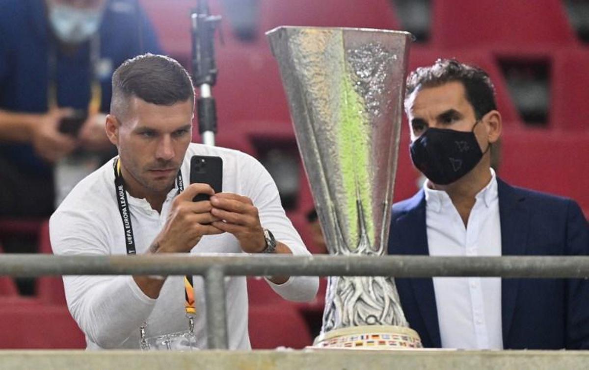 German football player Lucas podolski (L) photographs the trophy prior to the UEFA Europa League semi-final football match Sevilla v Manchester United on August 16, 2020 in Cologne, western Germany. Martin Meissner / POOL / AFP