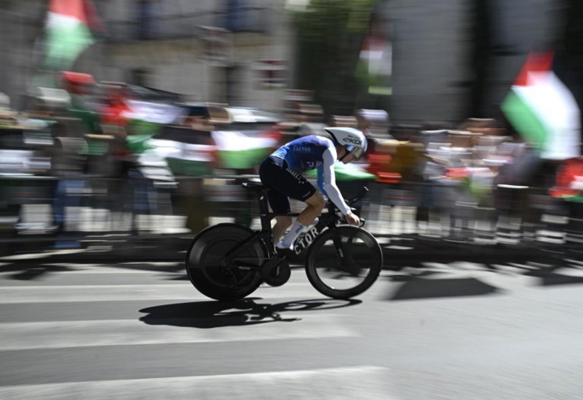 Pro-Palestinians protesters wave Palestinian flags as Team Israel Premier Tech 's British rider Jake Stewart competes during the 18th stage of the Vuelta a Espana, a 26 km race against the clock between Valladolid and Valladolid, on September 11, 2025. Miguel RIOPA / AFP