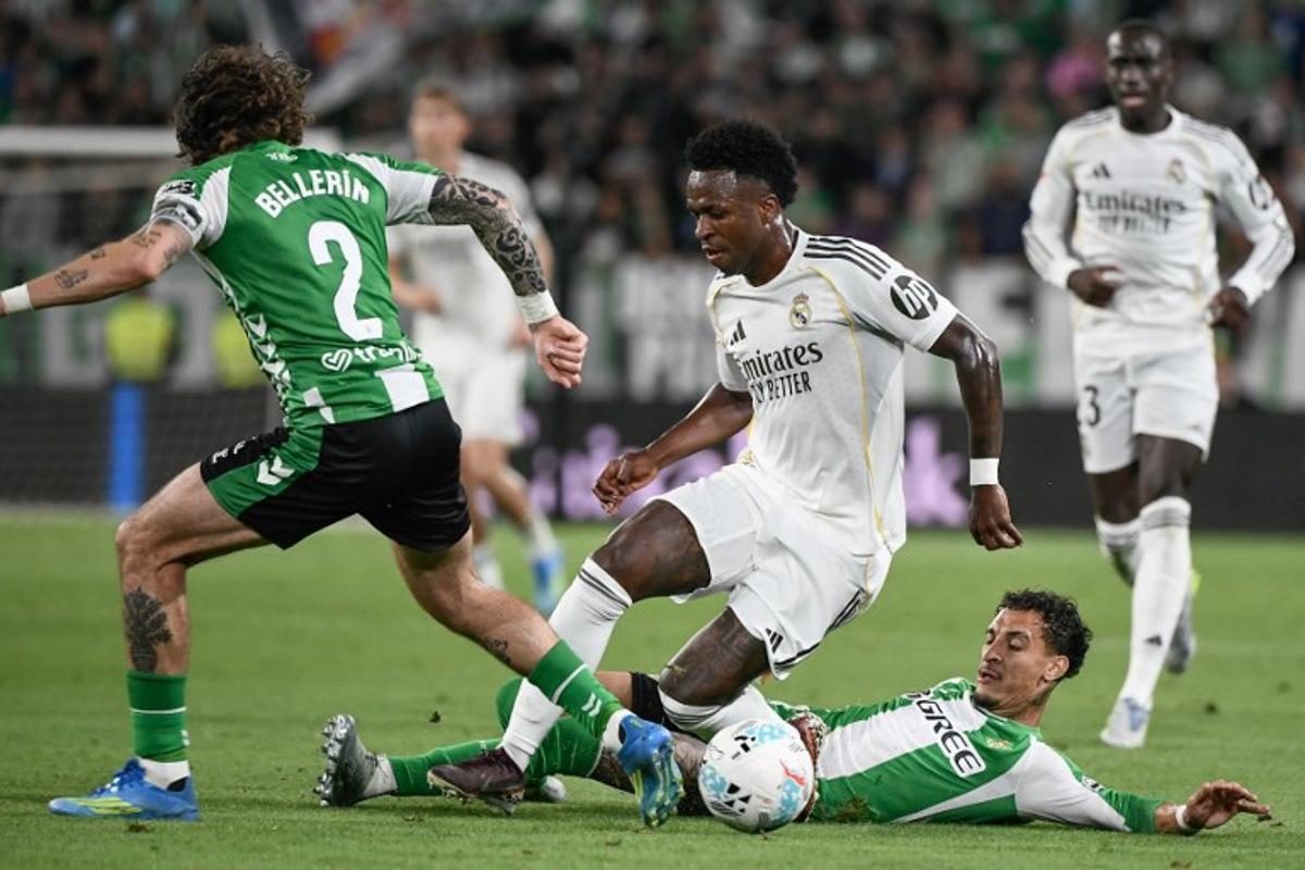 Real Madrid's Brazilian forward #07 Vinicius Junior (C) vies for the ball with Real Betis' Brazilian forward #07 Antony (R) and Real Betis' Spanish defender #02 Hector Bellerin during the Spanish league football match between Real Betis and Real Madrid CF at the La Cartuja stadium in Seville on April 24 , 2026. CRISTINA QUICLER / AFP
