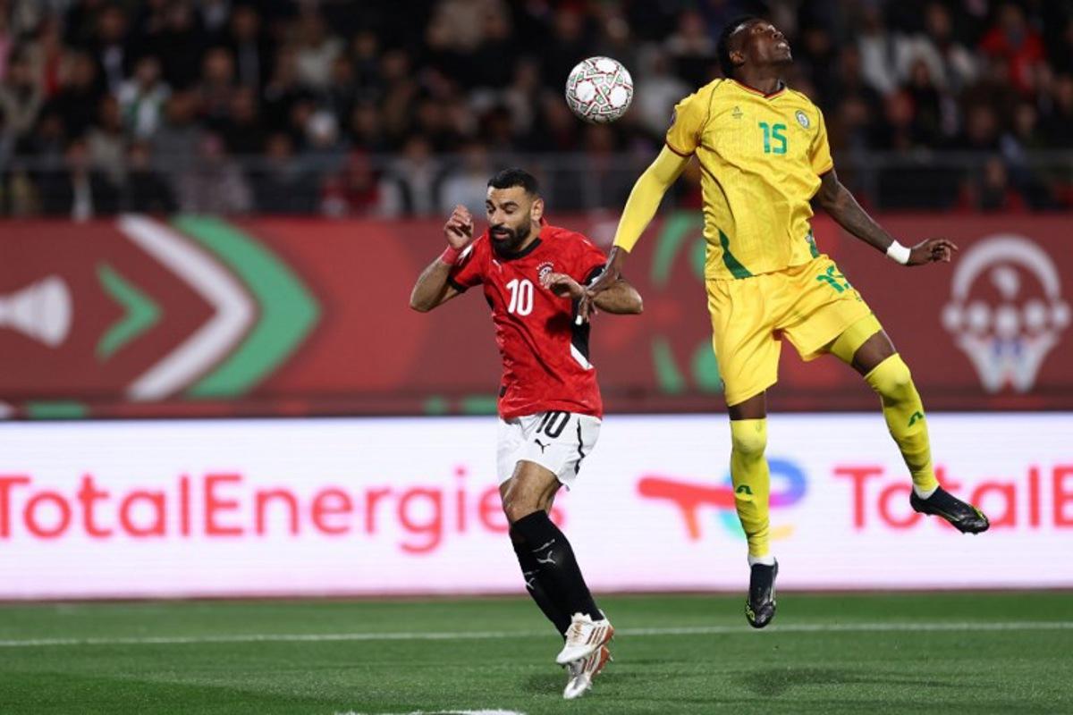 Egypt's forward #10 Mohamed Salah and Zimbabwe's defender #15 Teenage Hadebe jump for the ball during the Africa Cup of Nations (CAN) group B football match between Egypt and Zimbabwe at Adrar Stadium in Agadir on December 22, 2025. FRANCK FIFE / AFP