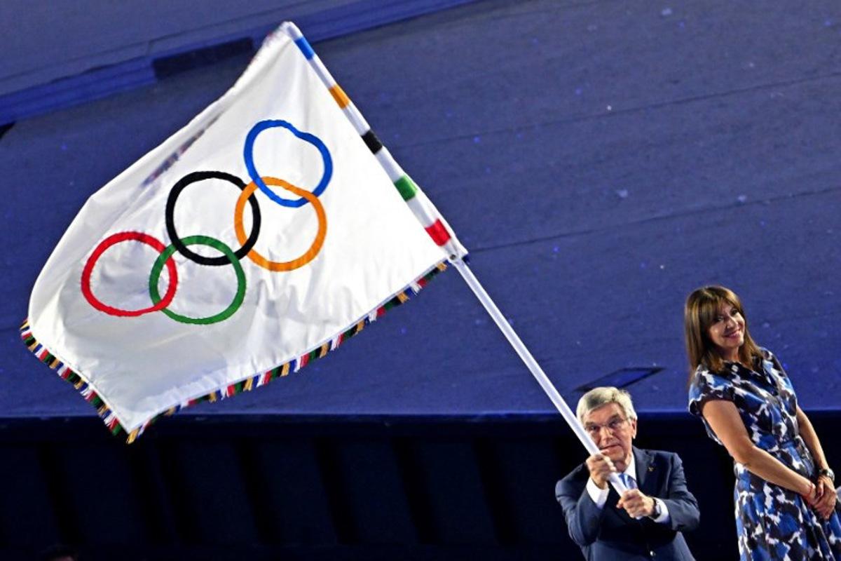 International Olympic Committe (IOC) President Thomas Bach (L) waves the Olympic flag next to Paris' Mayor Anne Hidlago during the handing of the flag as part of the closing ceremony of the Paris 2024 Olympic Games at the Stade de France, in Saint-Denis, in the outskirts of Paris, on August 11, 2024. Miguel MEDINA / AFP