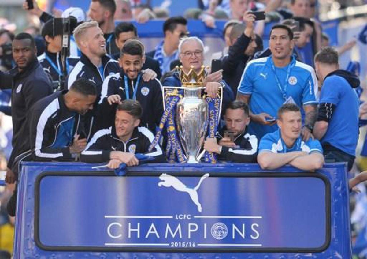 (L-R) Leicester City's English defender Wes Morgan, Leicester City's Danish goalkeeper Kasper Schmeichel, Leicester City's Algerian midfielder Riyad Mahrez, Leicester City's Italian manager Claudio Ranieri, Leicester City's English midfielder Danny Drinkwater, Leicester City's Argentinian striker Leonardo Ulloa and Leicester City's German defender Robert Huth stand with the Premier league trophy as the Leicester City team take part in an open-top bus parade through Leicester to celebrate winning the Premier League title on May 16, 2016. / AFP PHOTO / GLYN KIRK