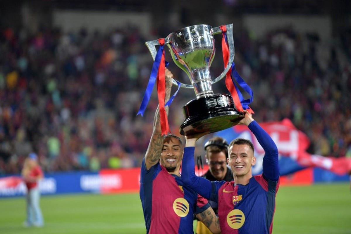 Barcelona's Brazilian forward #11 Raphinha (L) and Barcelona's Spanish midfielder #17 Marc Casado raise their trophy as they celebrate their 28th Liga title after the Spanish league football match between FC Barcelona and Villarreal CF at Estadi Olimpic Lluis Companys in Barcelona on May 18, 2025. MANAURE QUINTERO / AFP