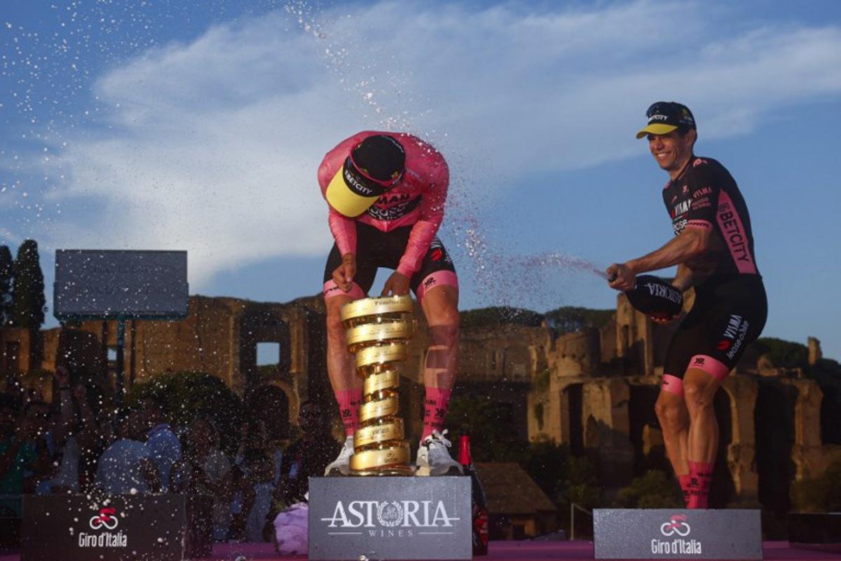 Team Visma-Lease a Bike's British rider Simon Yates (L) wearing the pink jersey of overall leader (Maglia Rosa) celebrates holding the Trofeo Senza Fine on the podium with teammate Team Visma-Lease a Bike's Belgian rider Wout Van Aert after the 21st and last stage and winning the 108th Giro d'Italia cycling race of 143kms from Rome to Rome on June 1, 2025. Luca Bettini / AFP
