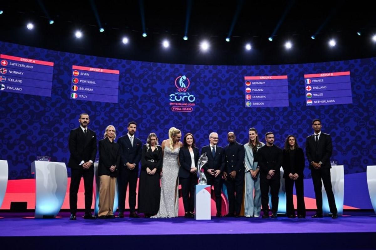 (From L) Italian former football player Leonardo Bonucci, Former Swiss football player Caroline Seger, German former football player Sami Khedira, TV host and Swiss sports presenter Annette Fetscherinas, UEFA head of women's football and German former football player Nadine Kessler, UEFA's Deputy General Secretary Giorgio Marchetti, TV host and former English football player Ian Wright, English former football player Jill Scott, Swiss football player Xherdan Shaqiri, Spanish football forward Veronica Boquete and French former football player Raphael Varane pose in front of a screen displaying fixtures of the group stage of the UEFA Women's Euro 2025 trophy after the draw in Lausanne, on December 16, 2024. Fabrice COFFRINI / AFP