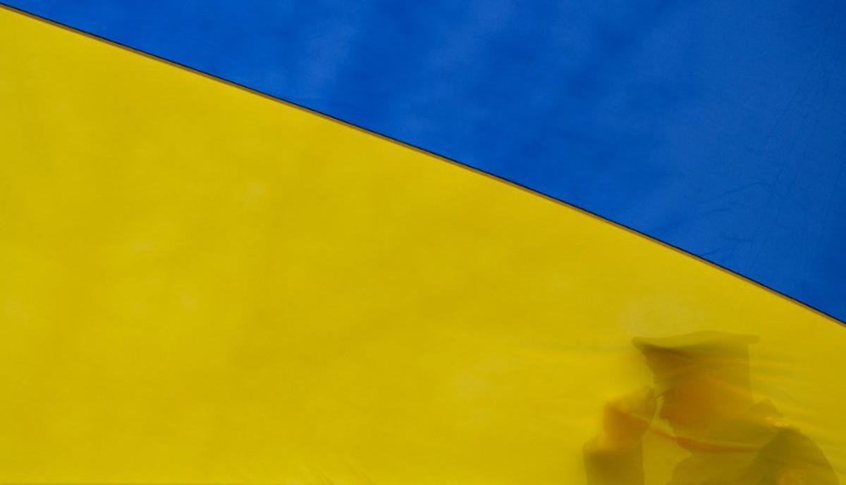 A Ukrainian serviceman sets his cap straigh as he participates in holding the national flag beore it raises to the flagpole during a ceremony marking the first anniversary of the retreat of Russian troops from the Ukrainian town of Bucha, in Bucha, near Kyiv, on March 31, 2023. Sergei SUPINSKY / AFP