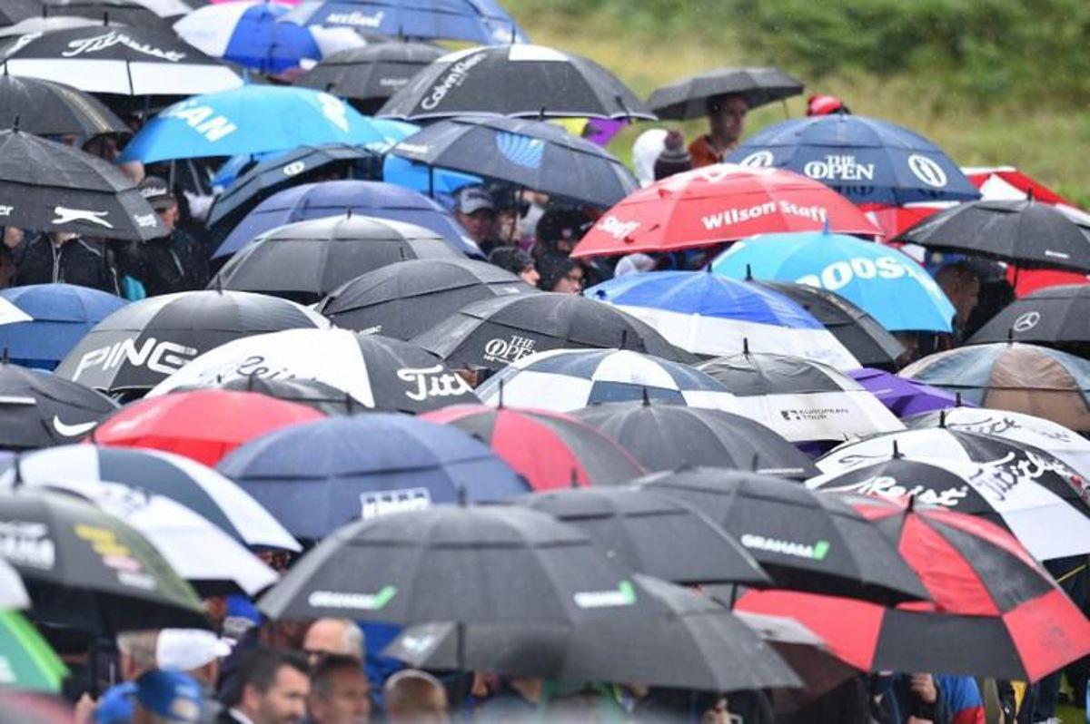 Spectators shelter under umbrellas during the second round of the British Open golf Championships at Royal Portrush golf club in Northern Ireland on July 19, 2019. Glyn KIRK / AFP RESTRICTED TO EDITORIAL USE