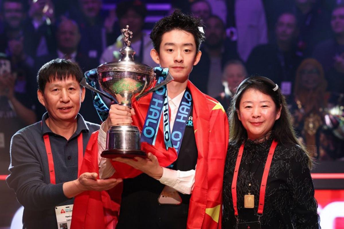 China's Wu Yize (C) holds the championship trophy as he poses with his parents during the awards ceremony after his victory over England's Shaun Murphy in the World Snooker Championship final round at The Crucible in Sheffield, northern England on May 4, 2026. Darren Staples / AFP