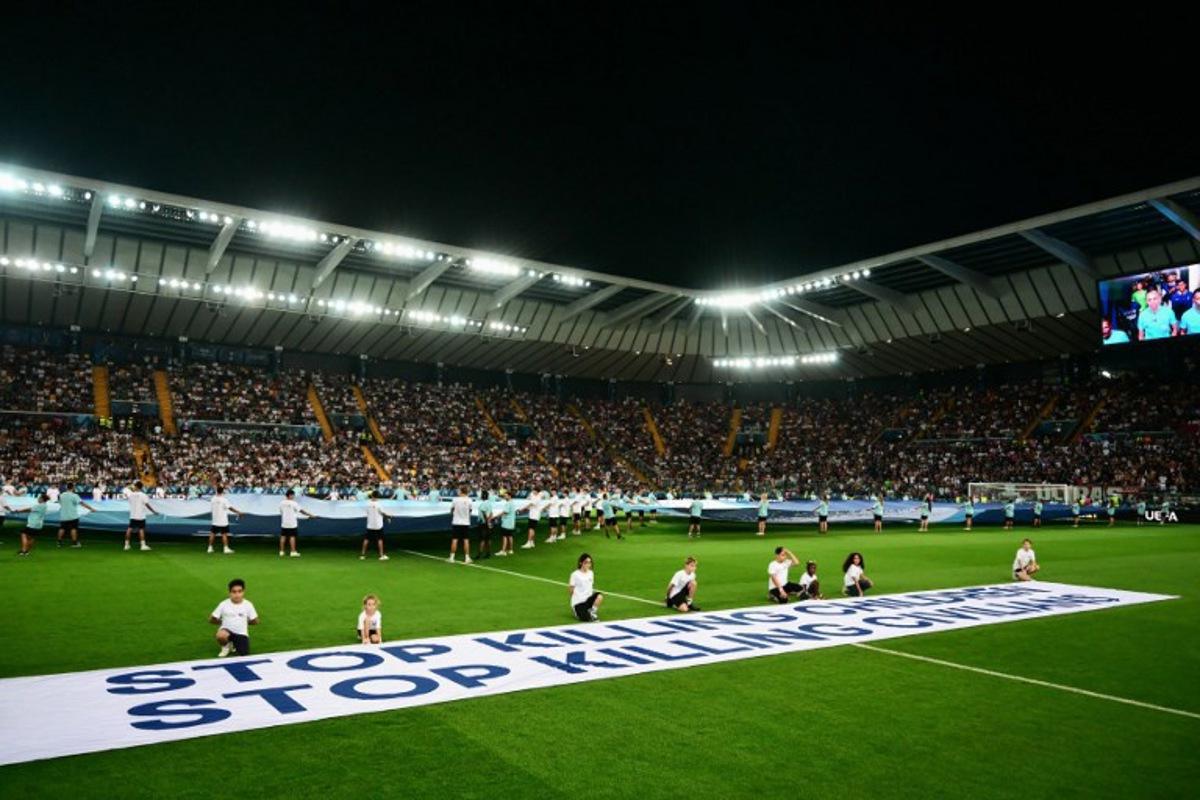 Mascots hold a banner which reads "Stop killing children, Stop killing civilians" on the pitch ahead of the 2025 UEFA Super Cup final football match between Paris Saint-Germain (FRA) and Tottenham Hotspur FC (ENG) at the Friuli stadium, in Udine, on August 13, 2025. Marco BERTORELLO / AFP