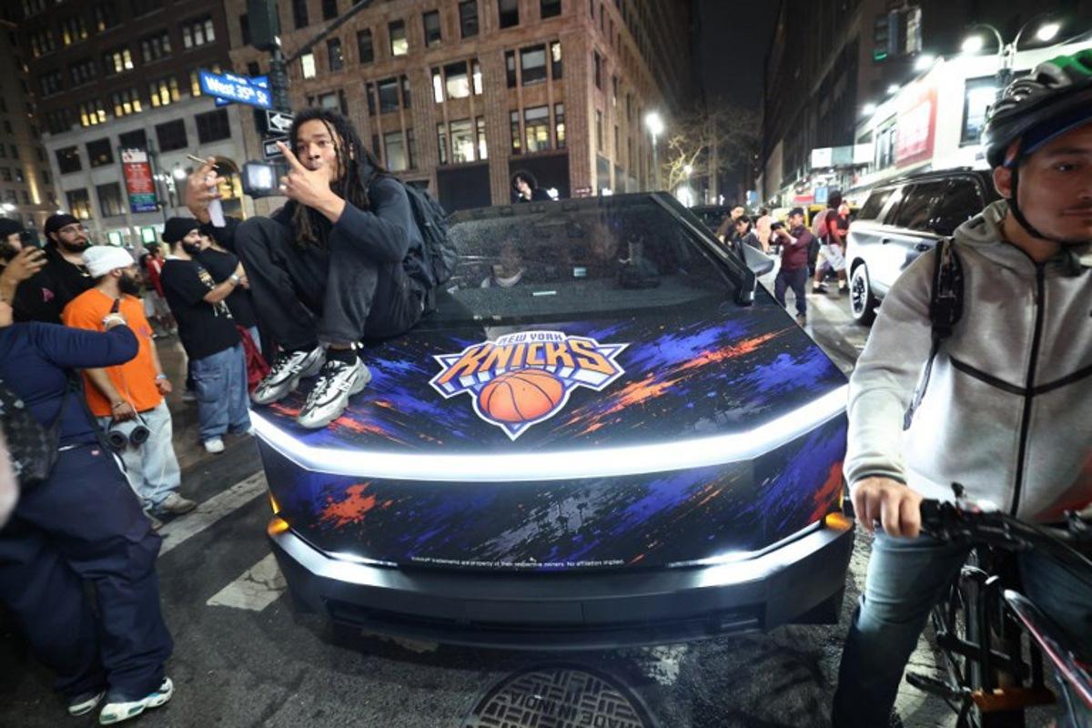 A Knicks fan sits on the hood of a car with Knicks stickers in New York, on June 10, 2026 during game four of the NBA Finals between the San Antonio Spurs and the New York Knicks. CHARLY TRIBALLEAU / AFP